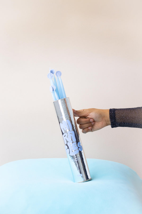 mano sosteniendo tubo plateado con letras azules y ocho velitas en su interior para ritual de luz 'Magnet for Miracles', perfectas para el Día de las Velitas en Colombia